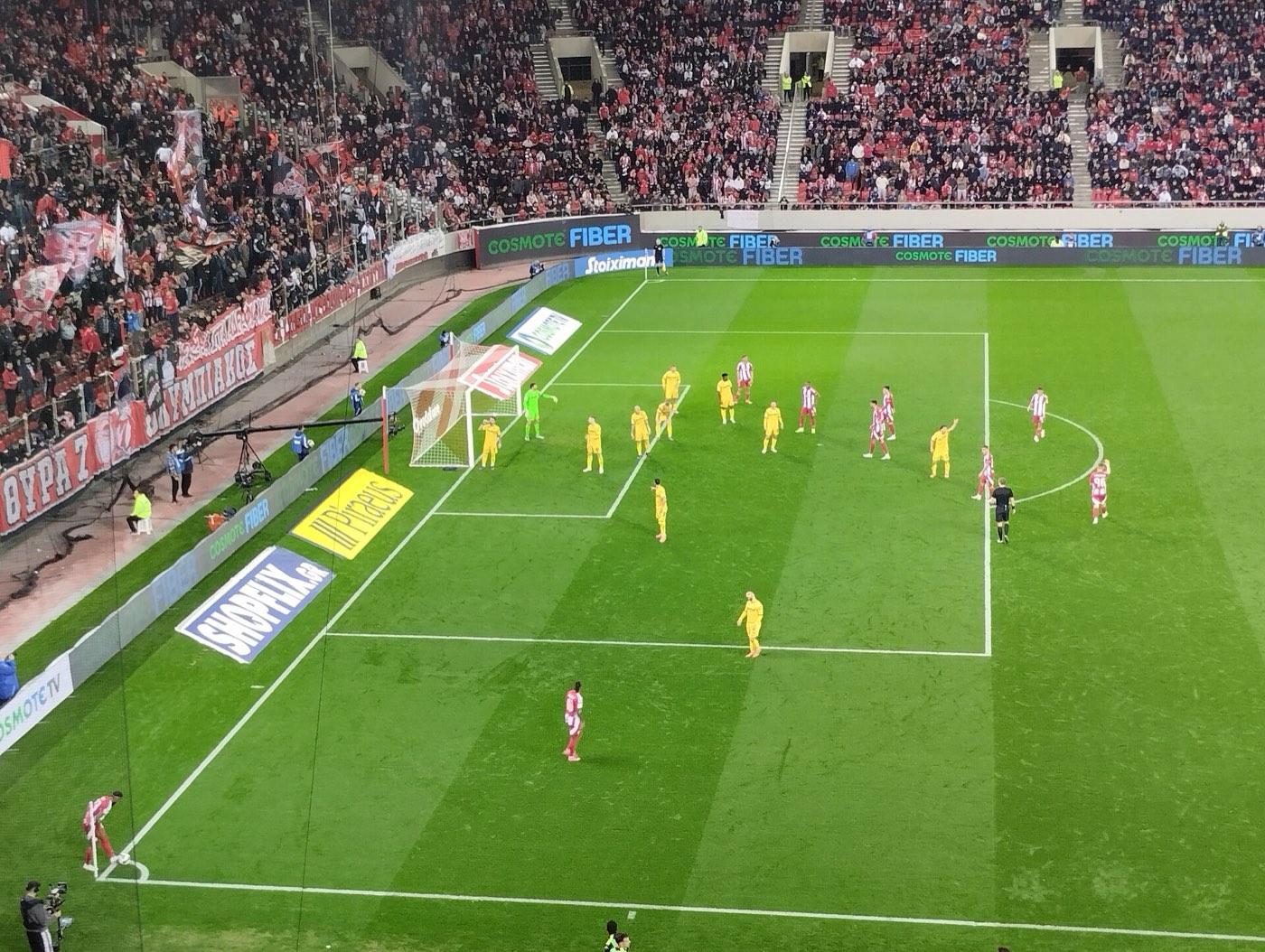 Olympiacos playing Aris at the Karaiskakis Stadium in Piraeus, with the stands full of fans in red and a Gate 7 banner along the front